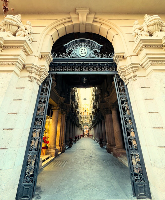Una puerta de hierro ornamentada abre paso a una galería de columnas y balcones en Albacete.