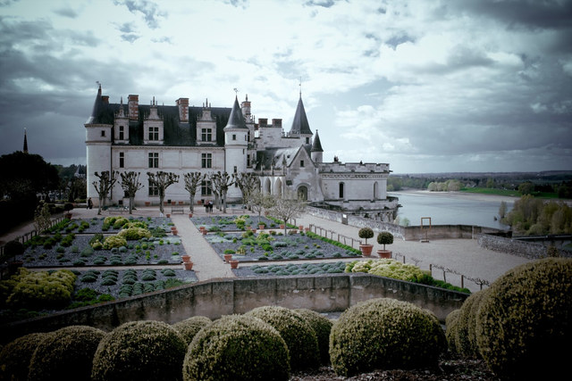 El castillo de Amboise domina jardines geométricos junto al río bajo un cielo cargado de nubes.
