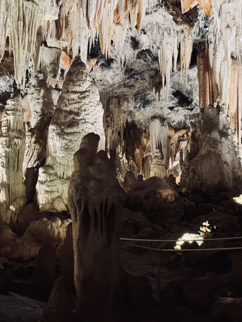 Estalactitas y estalagmitas iluminadas llenan una cueva de Ávila con formaciones blancas, ocres y oscuras.