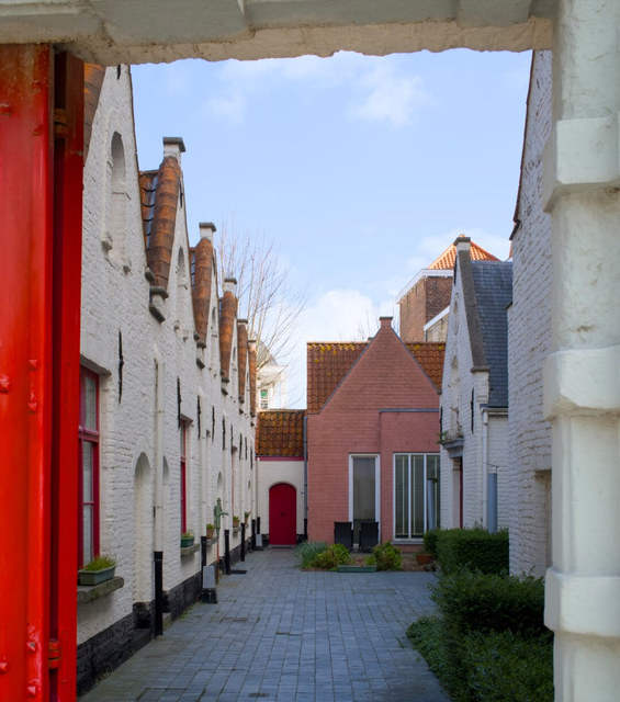 Un patio empedrado en Brujas queda enmarcado por casas blancas, puertas rojas y tejados escalonados.