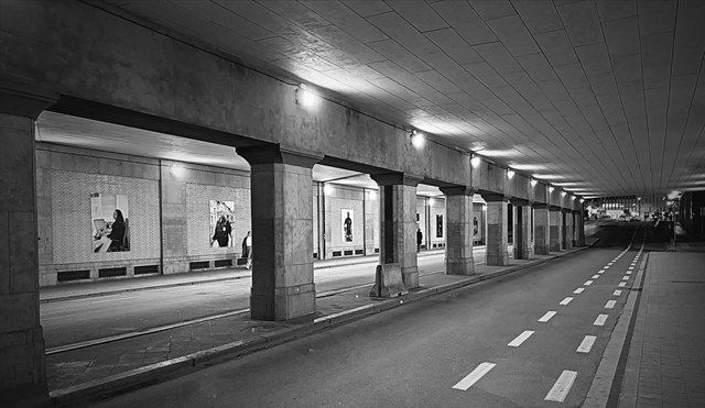 Una calzada vacía atraviesa un paso subterráneo de Bruselas, flanqueada por columnas, carteles iluminados y carriles discontinuos.
