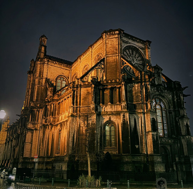 Una catedral gótica de Bruselas resalta bajo iluminación dorada nocturna, con rosetones, arbotantes y altos ventanales.