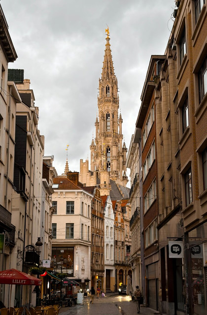 La torre gótica del Ayuntamiento de Bruselas domina una calle estrecha con terrazas y edificios históricos.