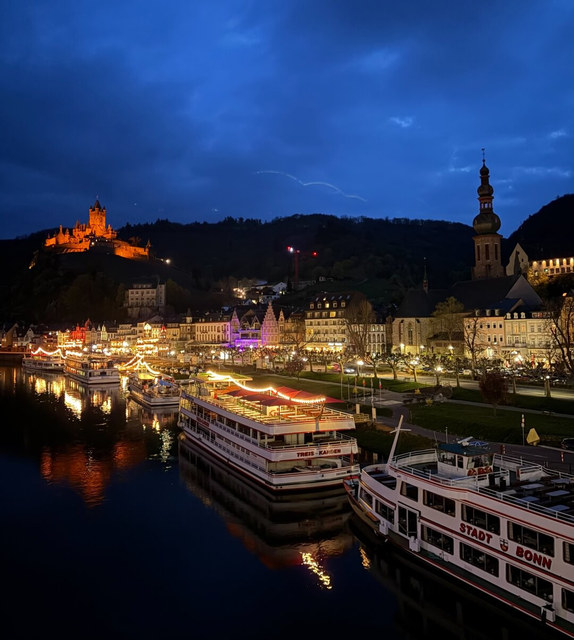 Barcos turísticos permanecen amarrados en Cochem mientras el castillo iluminado corona la colina al anochecer.
