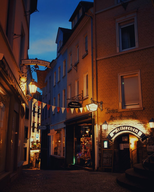 Faroles y luces de escaparates iluminan una calle estrecha de Cochem bajo el cielo azul del anochecer.