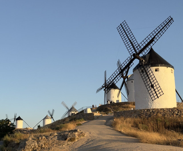 Molinos de viento blancos se alinean por una colina de Consuegra entre hierba seca y cielo despejado.