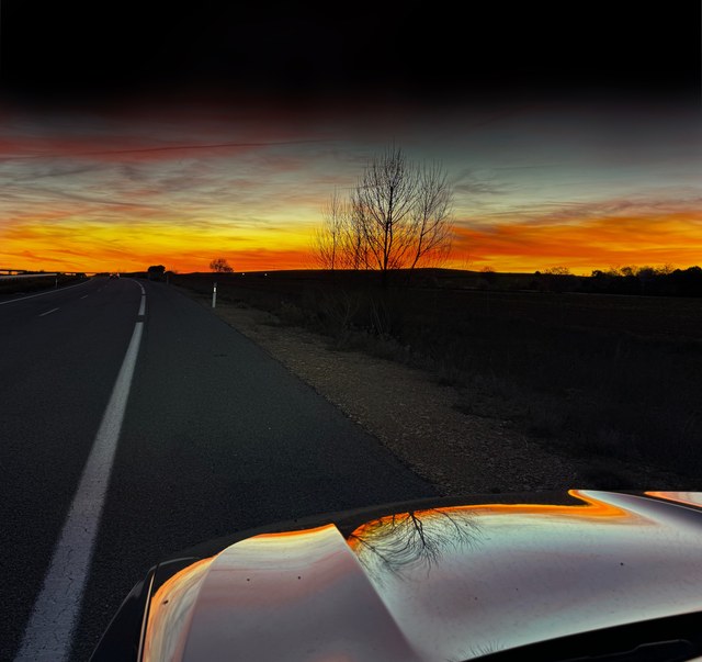 Una carretera recta avanza hacia un horizonte naranja mientras el atardecer se refleja sobre el capó en Cuenca.
