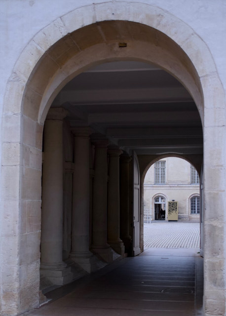 Un arco de piedra conduce desde un corredor sombreado hasta un patio luminoso de Dijon.