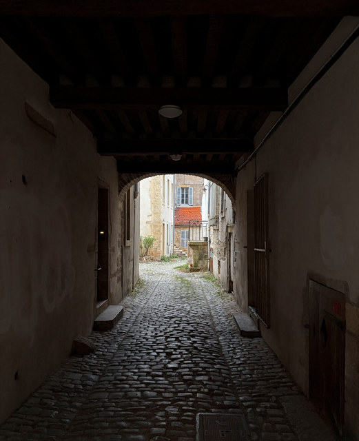 Un pasaje empedrado y oscuro desemboca en un patio luminoso entre fachadas antiguas de Dijon.