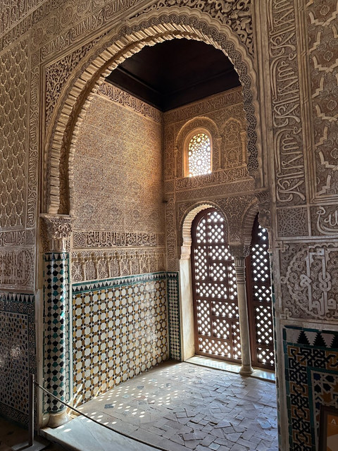 Arcos de herradura, yeserías árabes y azulejos geométricos cubren una estancia iluminada de la Alhambra.