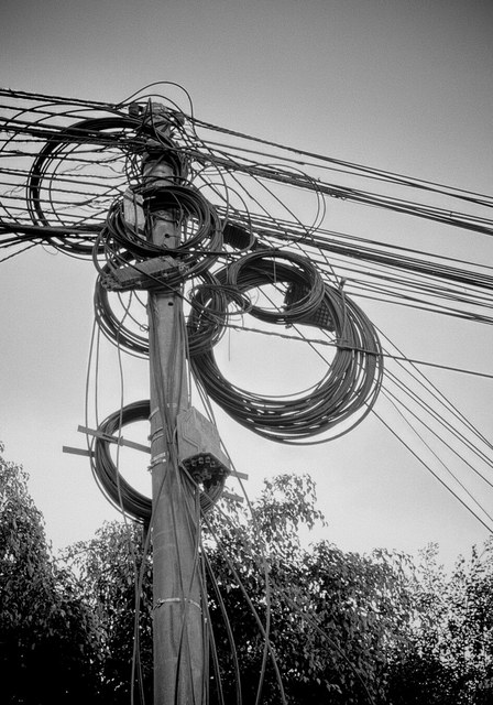 Un poste de Lima sostiene una maraña de cables eléctricos y grandes rollos suspendidos.