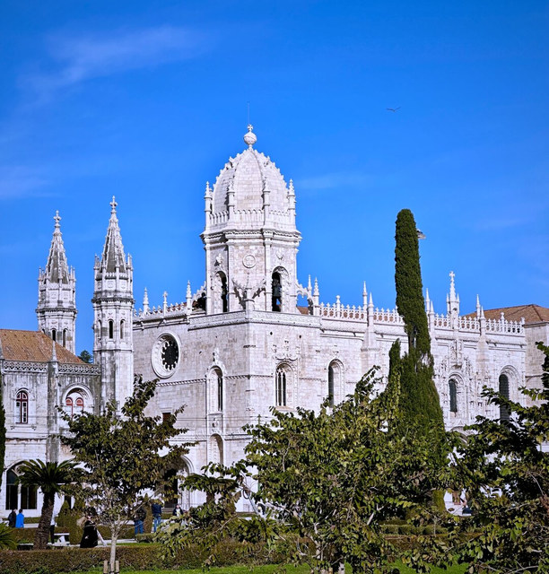 El monasterio de los Jerónimos se extiende tras un jardín, con un ciprés alto frente a su fachada.