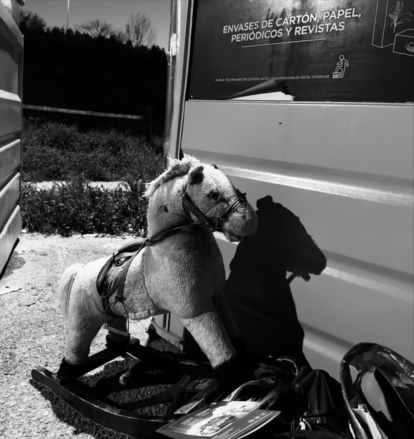 Un caballo balancín desgastado descansa junto a un contenedor de reciclaje y folletos esparcidos en Madrid.