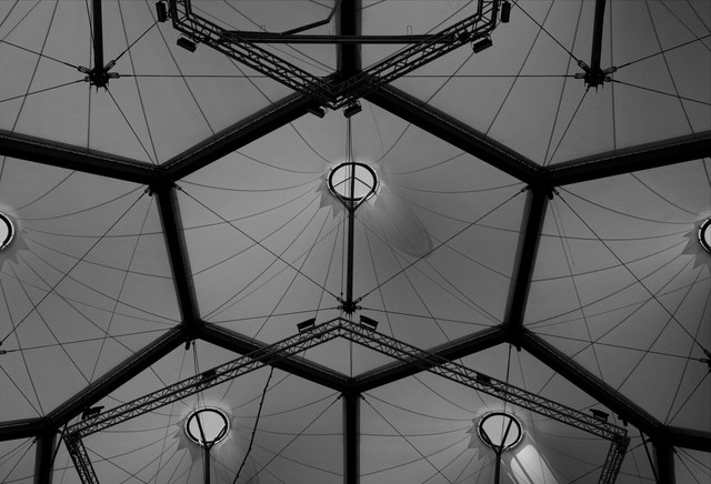 Una cubierta geométrica de membranas triangulares reúne focos circulares, cables tensados y estructuras metálicas.
