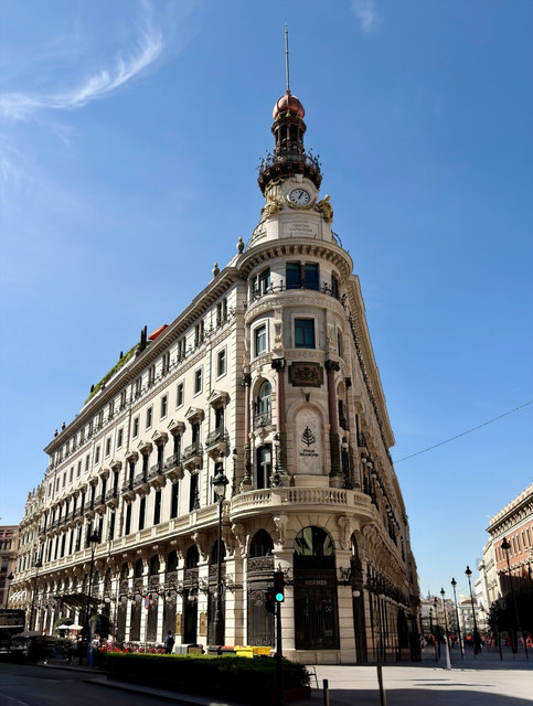 Un edificio blanco de esquina estrecha culmina en una torre con reloj sobre los escaparates de Hermès.