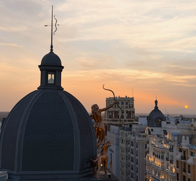 Una estatua dorada de arquera apunta al sol poniente junto a una gran cúpula de pizarra.