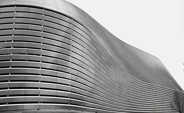 La fachada curva de un edificio moderno forma ondas continuas mediante largas franjas horizontales de metal.