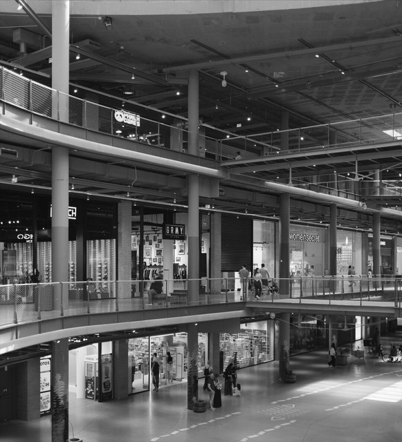 Varias plantas de un centro comercial madrileño conectan tiendas, pasarelas metálicas y compradores dispersos.