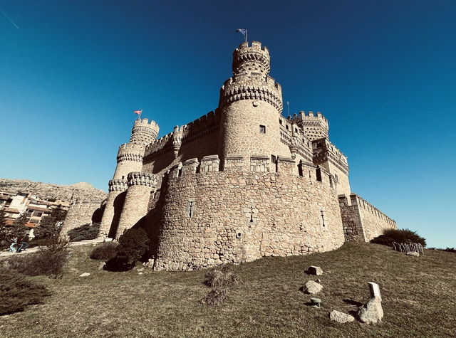 El castillo de Manzanares el Real presenta torres almenadas de piedra sobre una ladera bajo cielo azul.