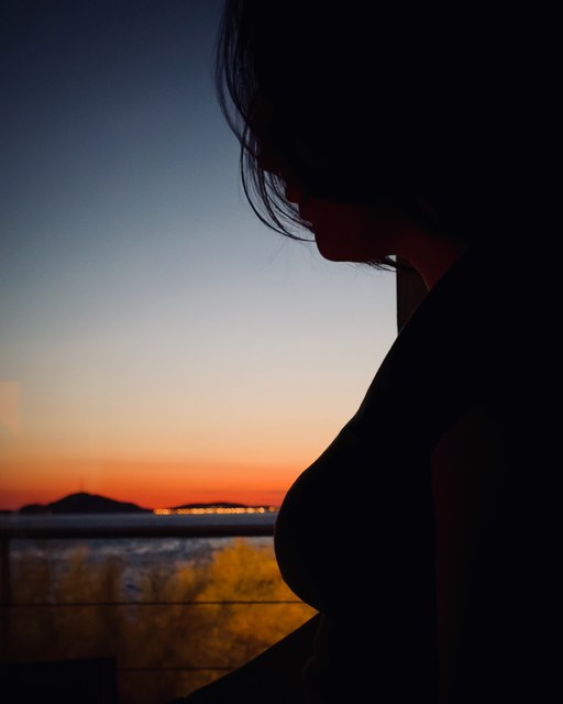 La silueta de una mujer aparece ante un ventanal durante el atardecer sobre el mar.