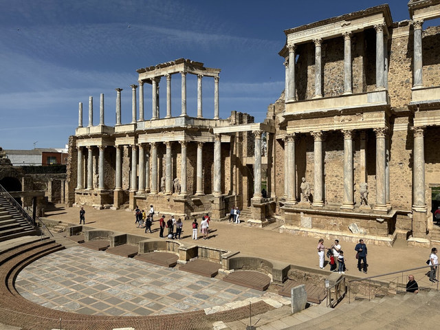 Columnas, estatuas y muros de piedra forman la escena del teatro romano de Mérida ante varios visitantes.