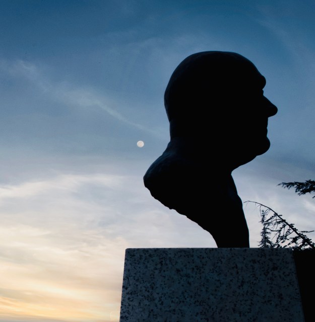 La silueta de un busto masculino recorta su perfil contra el cielo azul, con la luna visible detrás.