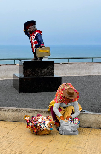 Una vendedora de Miraflores organiza muñecas artesanales junto a una estatua de oso con maleta.