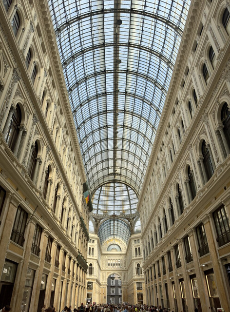 Una bóveda acristalada cubre la Galería Umberto I de Nápoles, flanqueada por fachadas ornamentadas y visitantes.