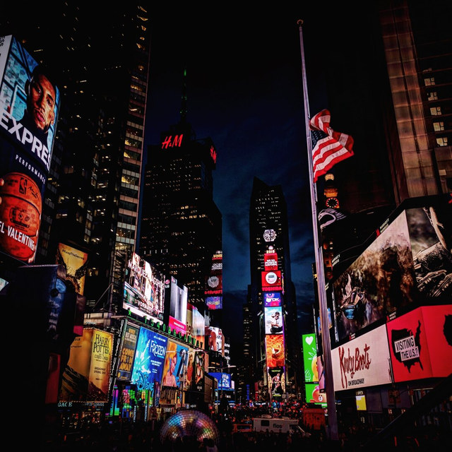 Pantallas publicitarias iluminan Times Square alrededor de una bandera estadounidense izada a media asta.