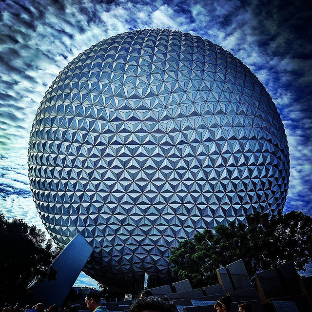 La esfera geodésica Spaceship Earth domina el encuadre sobre árboles y visitantes bajo nubes densas.