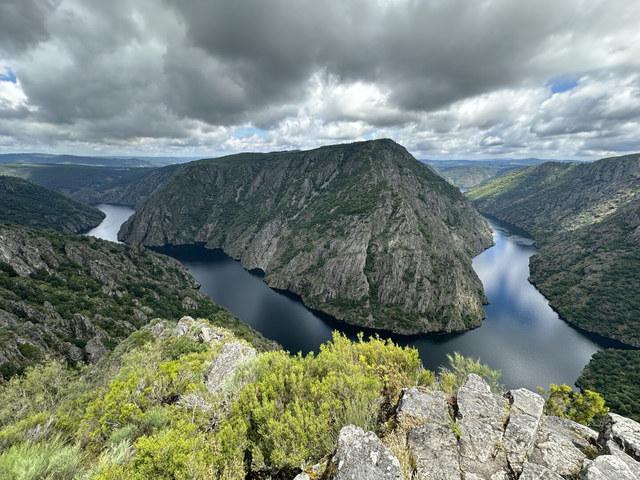 El río Sil rodea un macizo rocoso cubierto de vegetación bajo grandes nubes en Ourense.