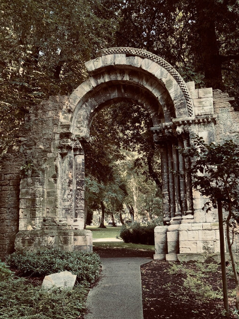 Un arco románico aislado enmarca un sendero entre árboles y arbustos de un parque de Oviedo.