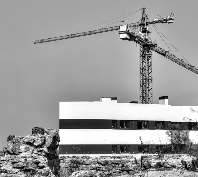 Grúas construyendo un edificio moderno tras el muro de piedra de un búnker de la Guerra Civil