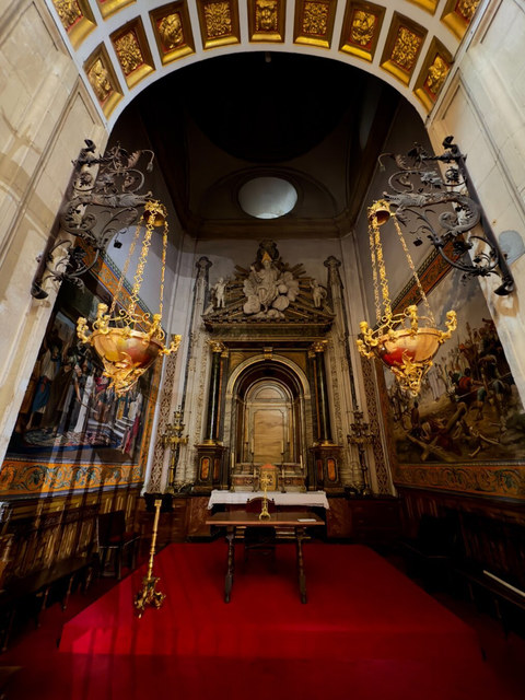 Dos lámparas doradas cuelgan ante un altar ornamentado, tapices laterales y una alfombra roja en Salamanca.
