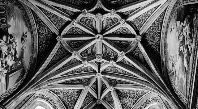 Una bóveda nervada despliega rosetones, relieves geométricos y pinturas laterales en blanco y negro.