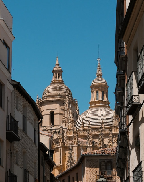 Las torres de la catedral de Segovia sobresalen entre fachadas estrechas bajo un cielo azul intenso.