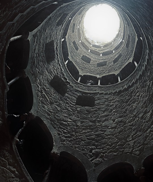 Una escalera de piedra asciende en espiral por el pozo iniciático de Sintra hacia una abertura luminosa.