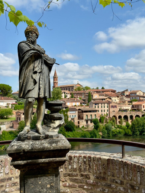Una estatua de bronce con capa y bastón se alza ante el río y los tejados de Toulouse.