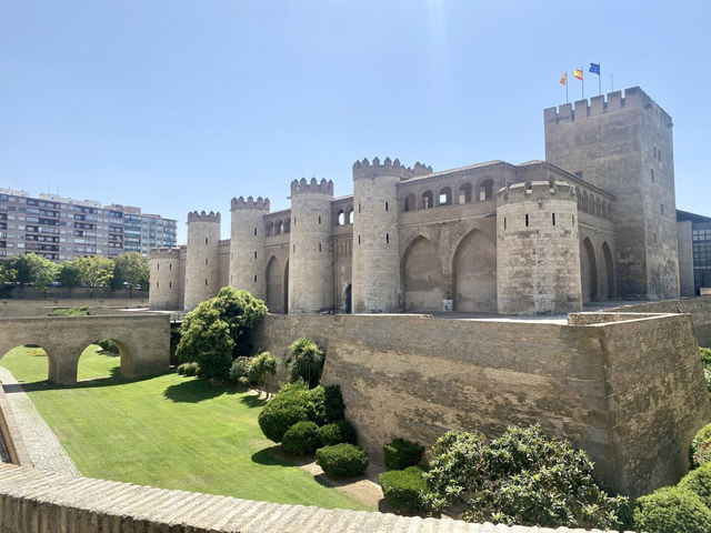 Torres semicirculares y murallas de piedra rodean el palacio de la Aljafería bajo el cielo despejado de Zaragoza.