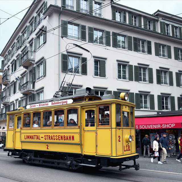 Un tranvía histórico amarillo circula por Zúrich con pasajeros a bordo y el pantógrafo conectado al tendido.